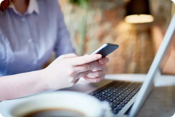 Person checking a phone next to a laptop in a cafe