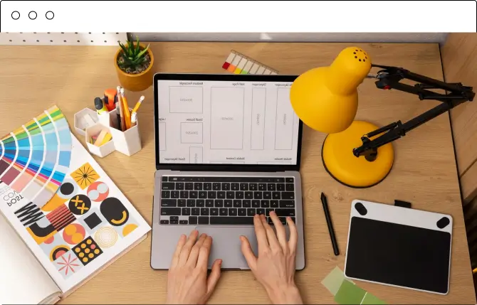 Designer's desk with a laptop showing website wireframes and a color palette