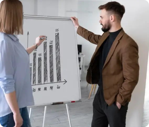 Two colleagues reviewing a sales chart on a whiteboard